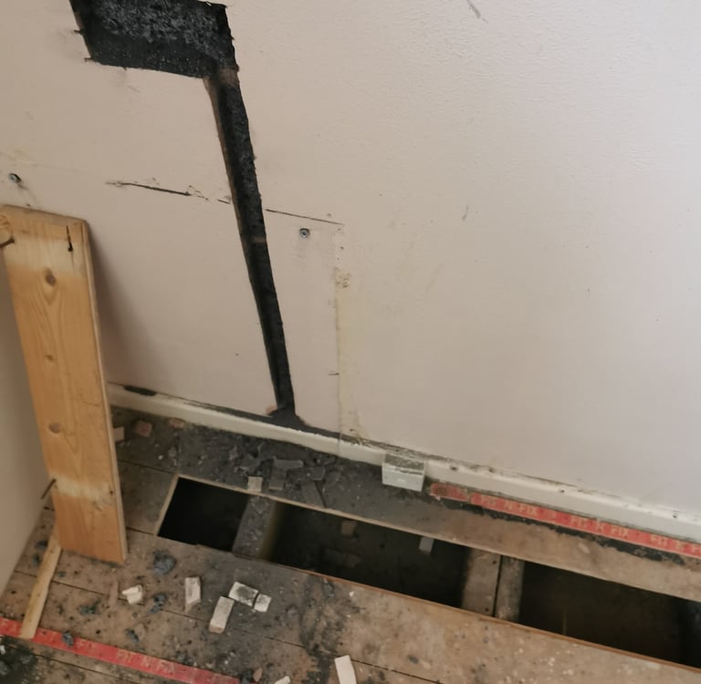 Wall cutout for electrical wiring above removed wooden floorboards.