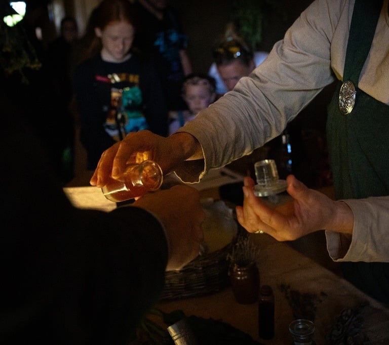 a person is holding a glass bottle places a drop of tincture onto the back of another person's hand