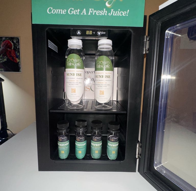 Crown TajisCafe fresh juice and infused spring water bottles in a black beverage refrigerator.