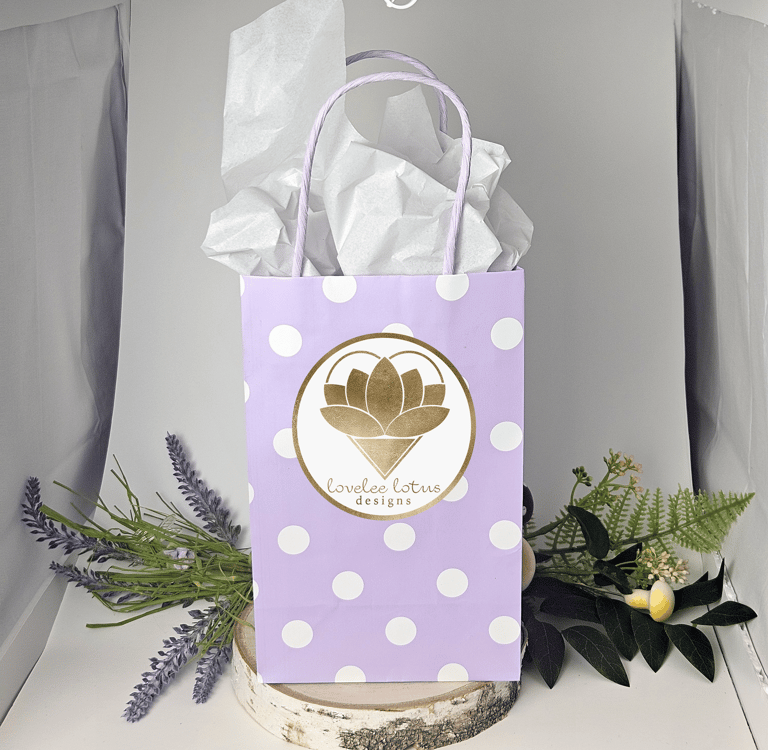 A purple gift bag with white dots and the Lovelee Lotus Designs logo