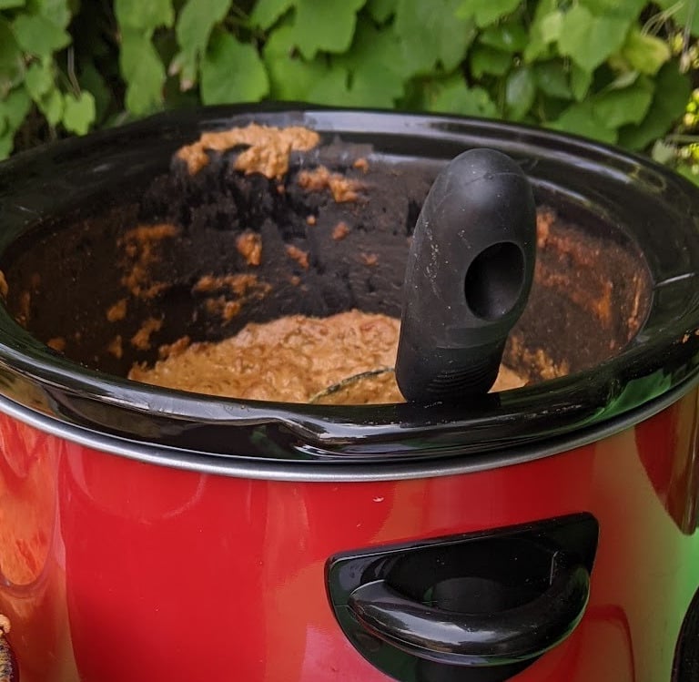 red and black crock pot with butter chicken inside