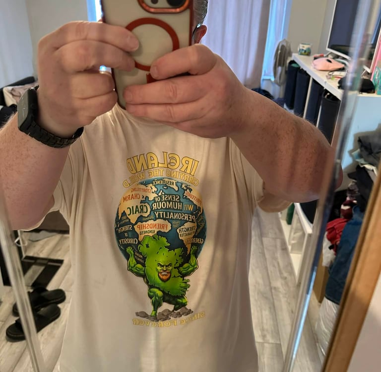 A man takes a mirror selfie wearing an off-white graphic t-shirt featuring a green Irish mythological figure.