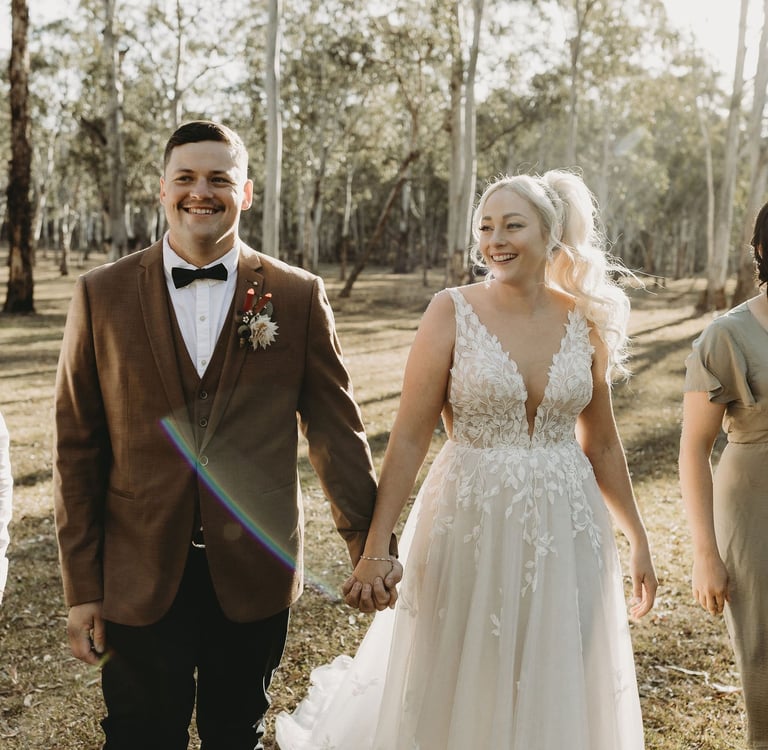 a bride and groom walking down a path in a wooded area