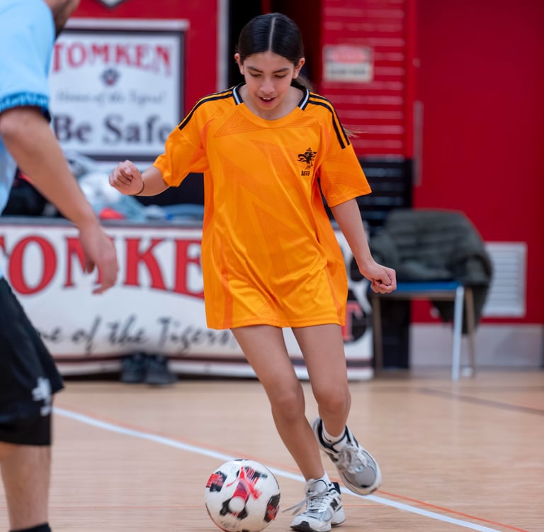 A young girl in a MVB FC Jersey dribbles a soccer ball indoor Mississauga Soccer School Practice