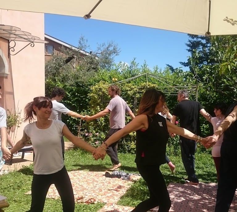 a group of people holding hands and dancing in a garden, classe di bioenergetica