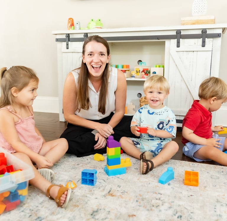 Therapist and a group of young children smiling at the camera, playing with blocks 