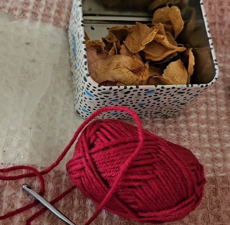 red yarn next to a crochet hook and dried rose petals
