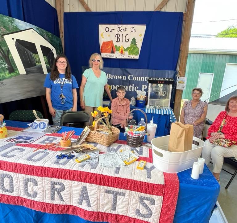 Five women sit or stand behind the Democrats booth at the fair