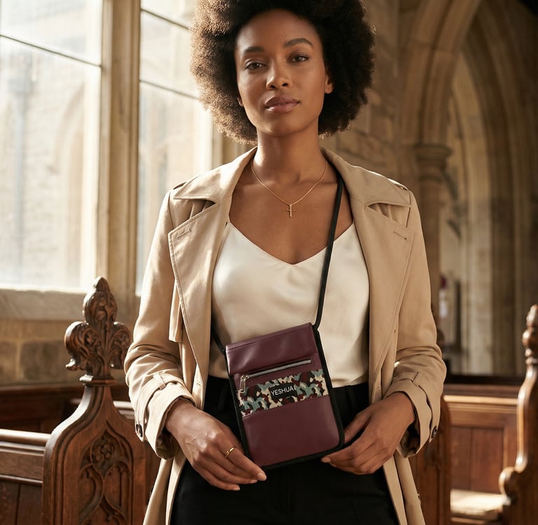 A stylish woman in a tan trench coat wearing a maroon crossbody travel neck wallet inside a church.