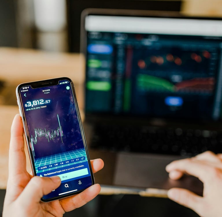 Pessoa analisando gráficos financeiros em um smartphone e um notebook