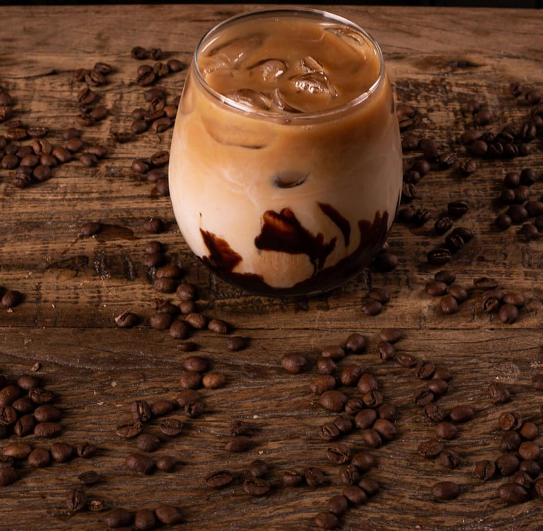 a glass of chocolate iced coffee on a table covered in coffee beans