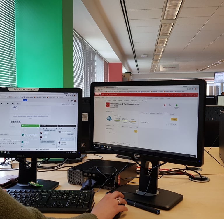 a woman sitting at a desk with two monitors and a keyboard