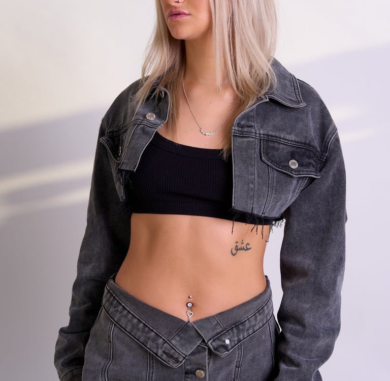 A blonde model wearing a black top and a grey denim cropped jacket and skirt