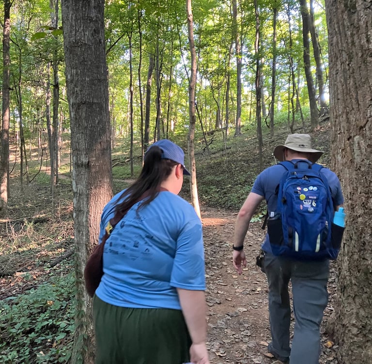A man and a woman hike up the dirt path in the woods