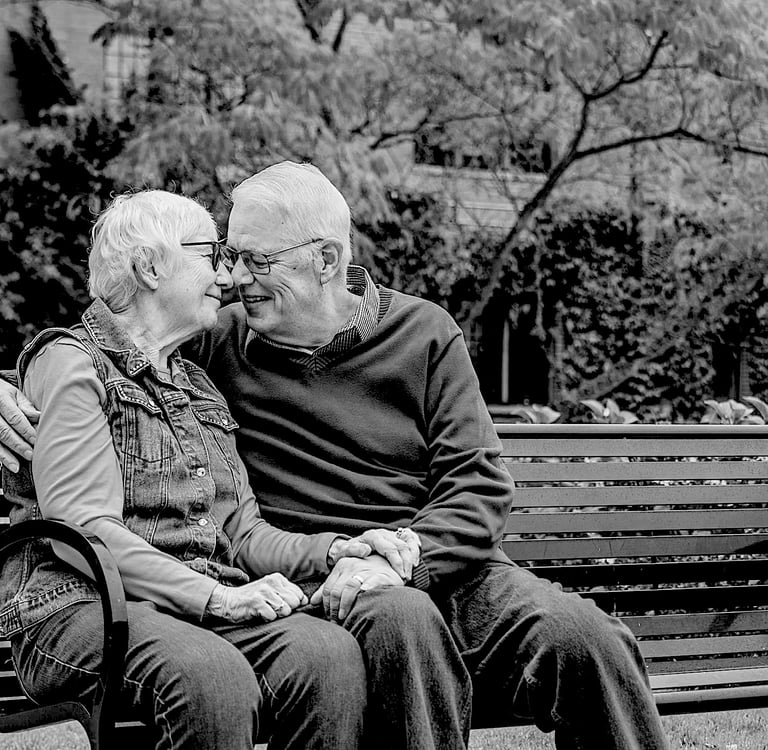 couple de personnes âgées se tenant la main, assis sur un banc