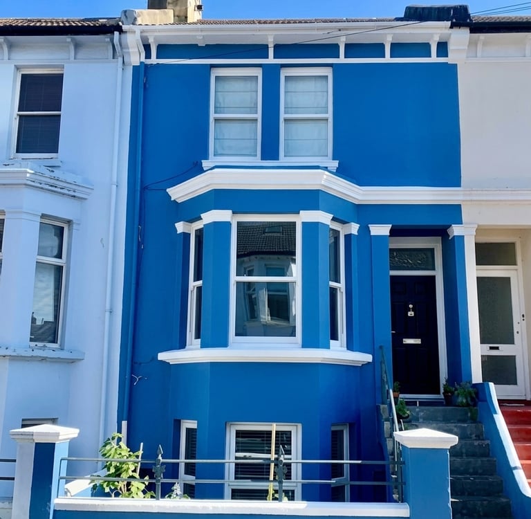 A vibrant blue terraced house with white trim and a large bay window in a residential Brighton area.