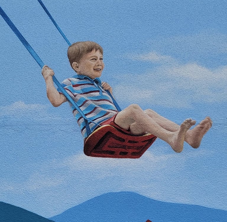 Fresque sur façade. Un garçon joue sur une balançoire au-dessus d'une pile de livres.