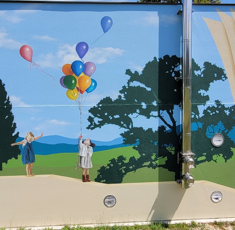 Fresque peinte sur façade. Des enfants jouent sur un muret, un paysage simplifié en arrière plan.