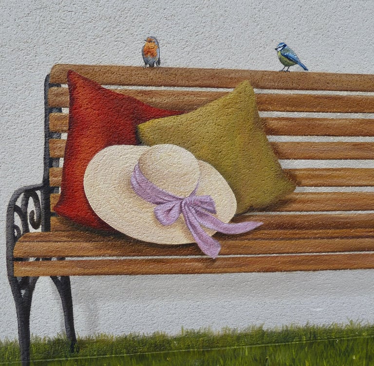 Détails d'une fresque peinte sur une façade. Tout est trompe-l'oeil: banc, oiseaux, herbe, livre,...