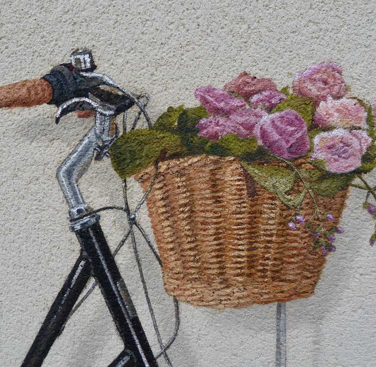 Détails d'un panier de vélo contenant des fleurs, peint en trompe-l'oeil sur une façade.