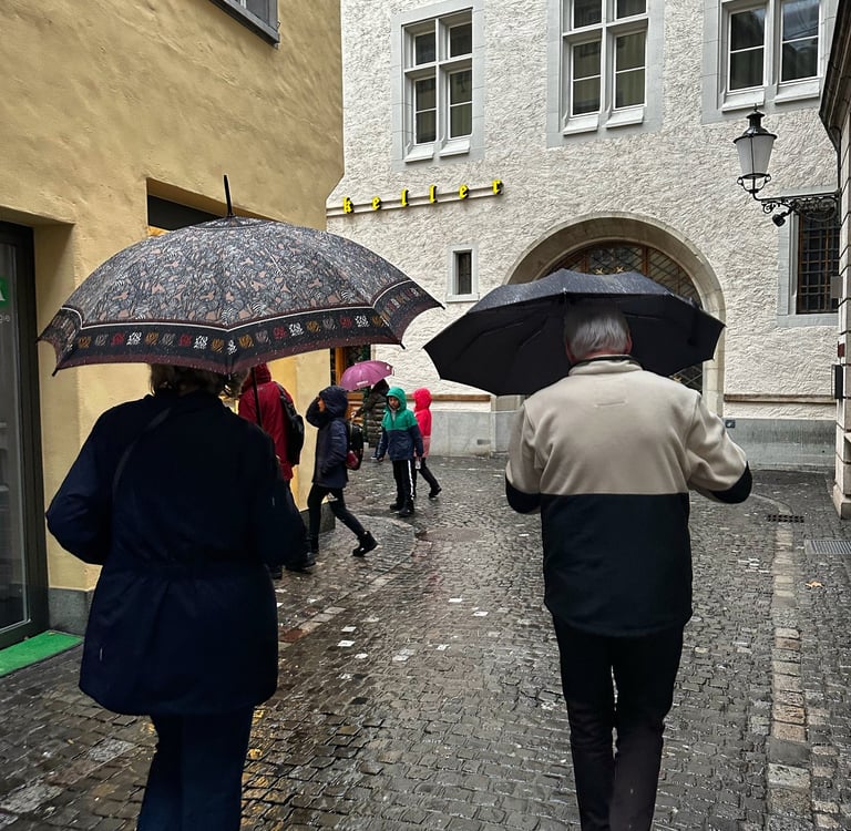 Rainy day in Switzerland, an older couple walk down the wet cobblestone roads together by LV