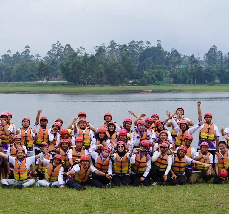 Sekelompok peserta rafting pangalengan berfoto bersama di tepi danau, mengenakan helm merah dan pelampung oranye,