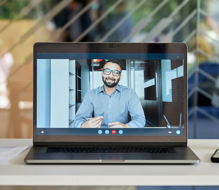 A laptop screen showing a video call with a man in a business shirt holding a pen