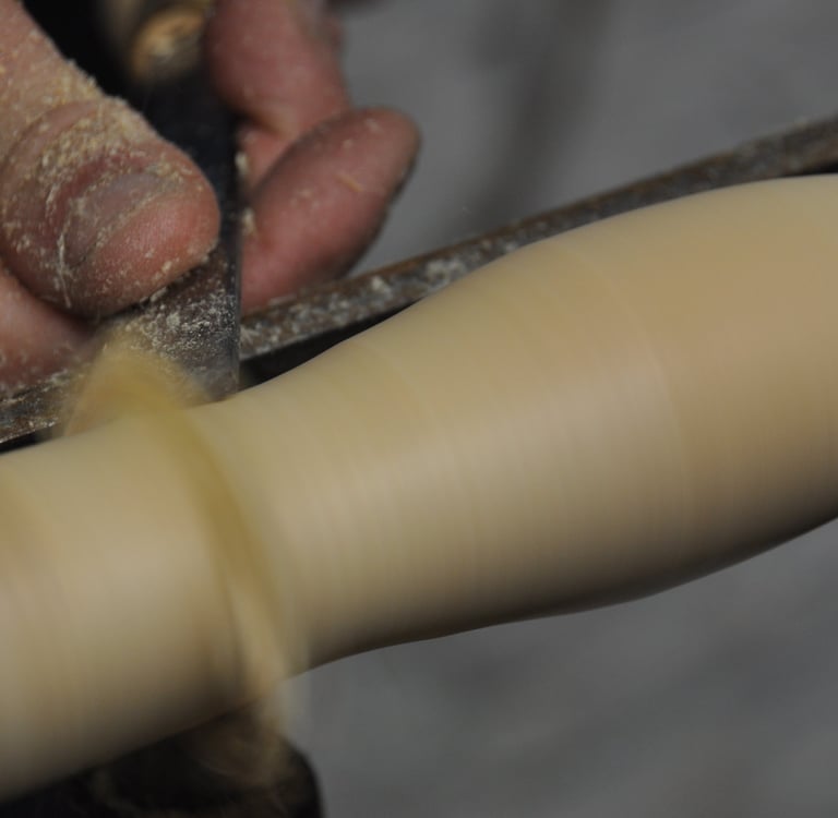 A close-up of a hand holding a chisel, turning wood spinning on a lathe