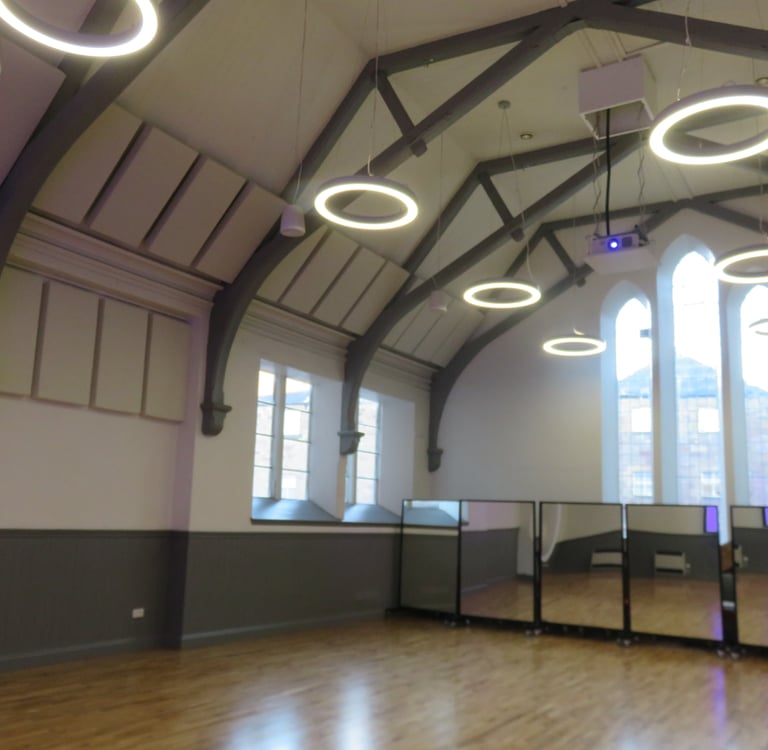 A large well-lit hall with a vaulted ceiling and large windows. It has a flat wood floor.