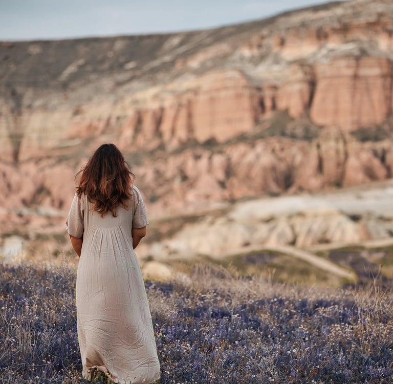 Woman in a beige dress standing in a lavender field with Cappadocia’s rock formations in the background