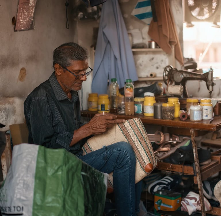 Elderly cobbler hand stitching leather bag in workshop, Mahebourg, Mauritius