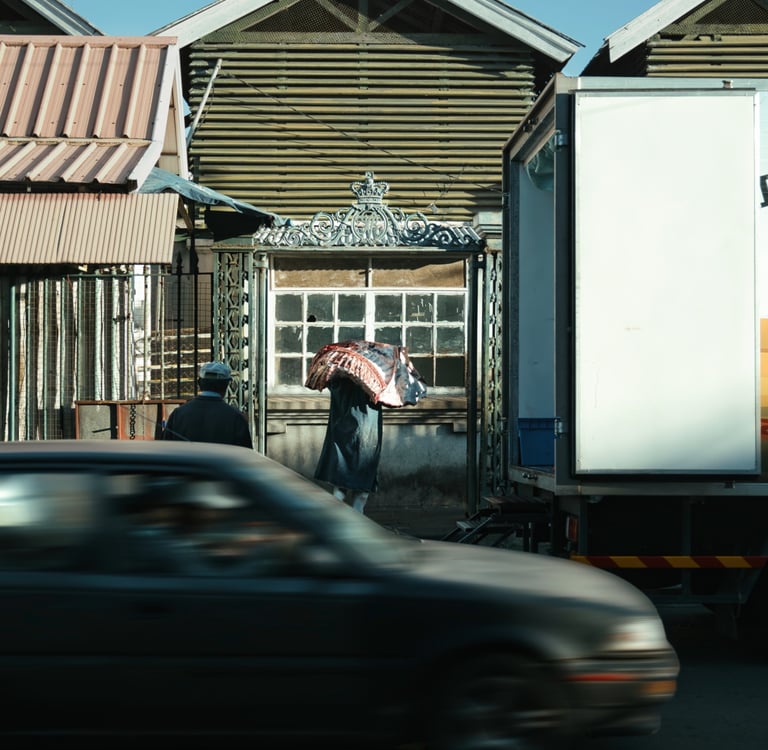 Worker carrying sack at rear entrance of Port Louis market, with passing cars