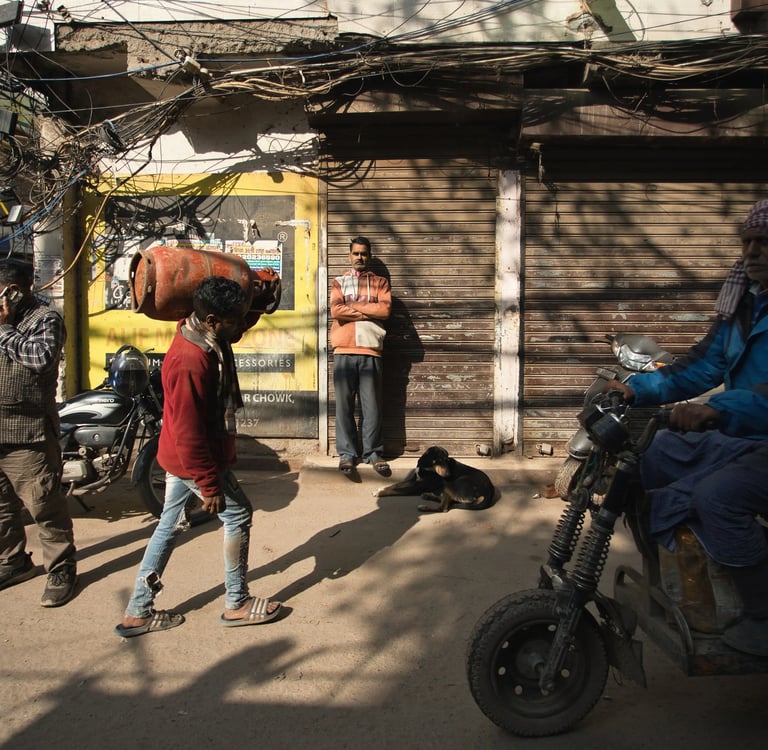 Pedestrians and a motorbike passing closed shops on an Old Delhi street.