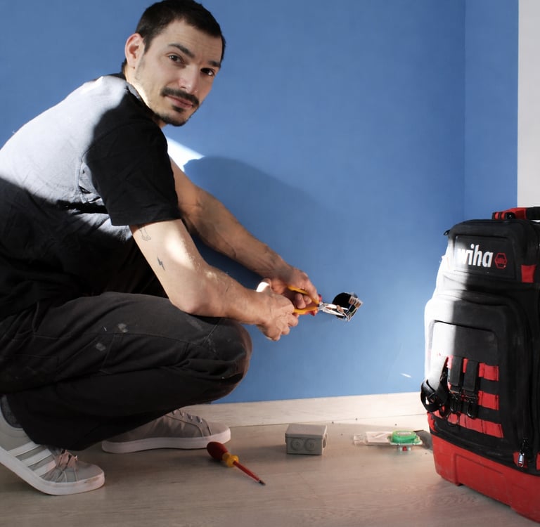 Professional electrician installing a wall socket using pliers near a Wiha tool backpack.