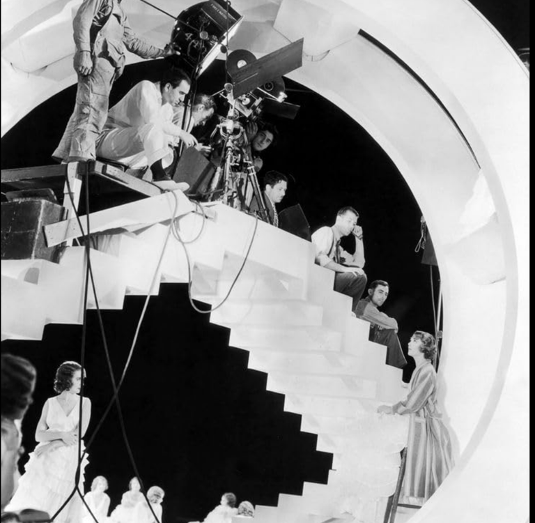 Busby Berkeley on a tall filming platform with cameras and lights, directing dancers below.