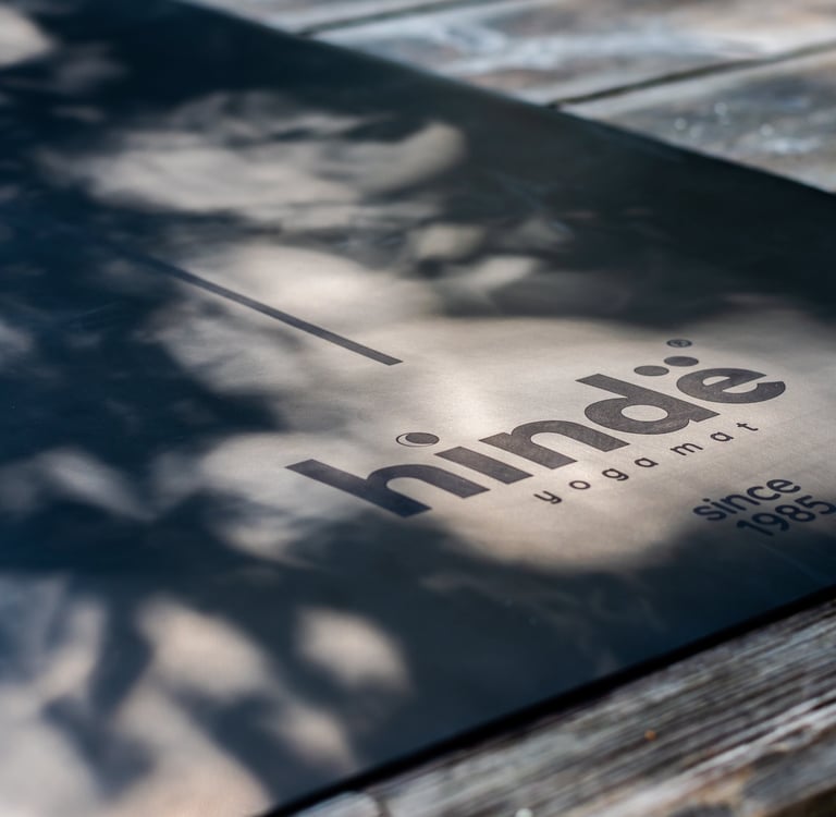 Black Hindie yoga mat with alignment lines on a rustic wooden deck with natural leaf shadows.
