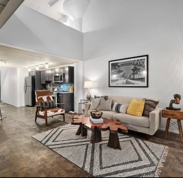 Modern industrial loft living room with live edge coffee table, beige sofa, and tripod floor lamp.