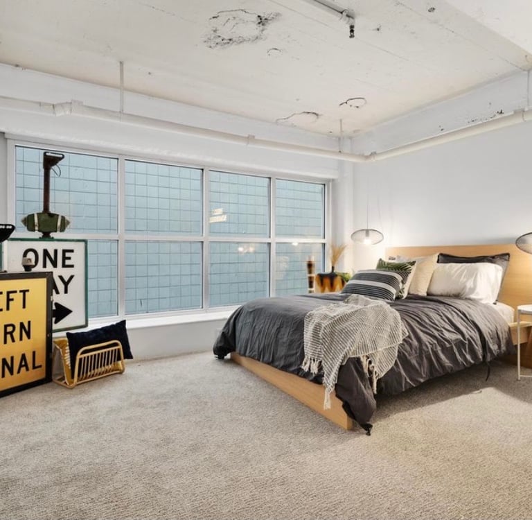 Modern industrial loft bedroom featuring a wooden bed, grey bedding, and vintage road signs.