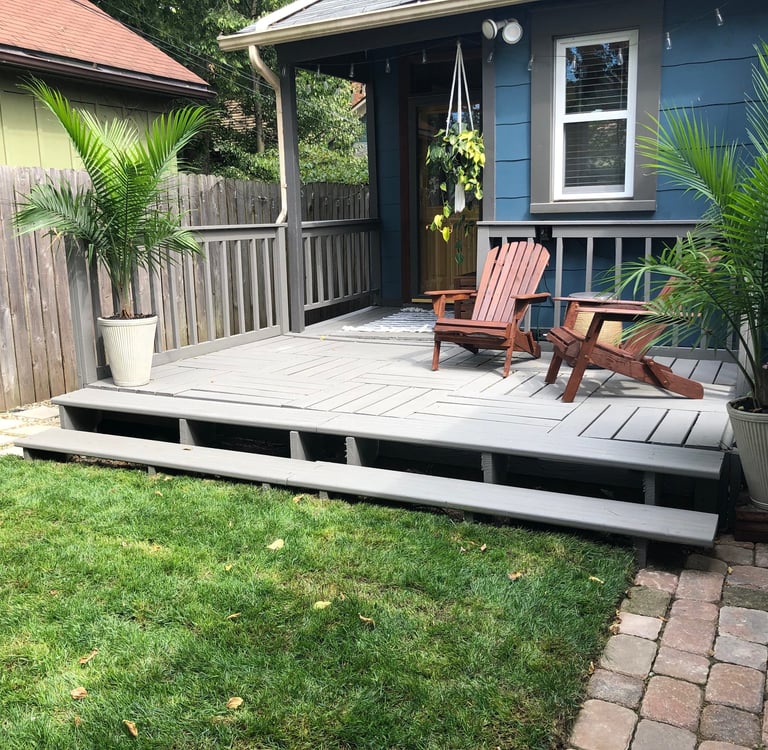 Backyard wooden deck with gray stain, Adirondack chairs, and potted palm trees.