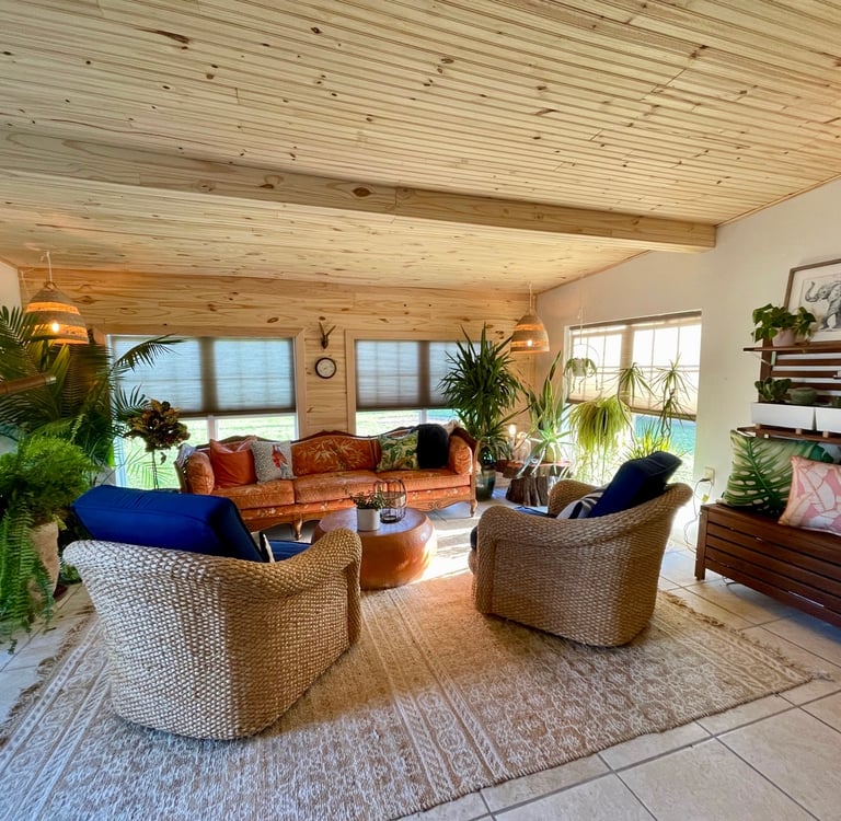 Boho sunroom interior with wood ceiling, wicker chairs, orange sofa, and many indoor plants.