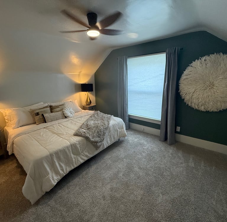 Modern bedroom with a white duvet, dark green accent wall, and a large feathery wall decor.