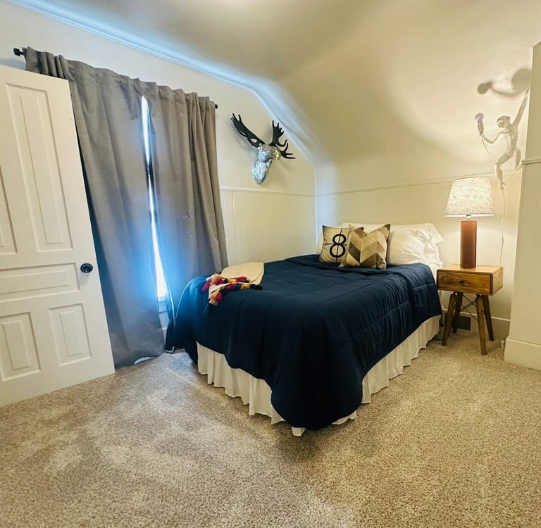 Cozy bedroom with a navy blue bed, silver moose head wall decor, and a wooden nightstand.