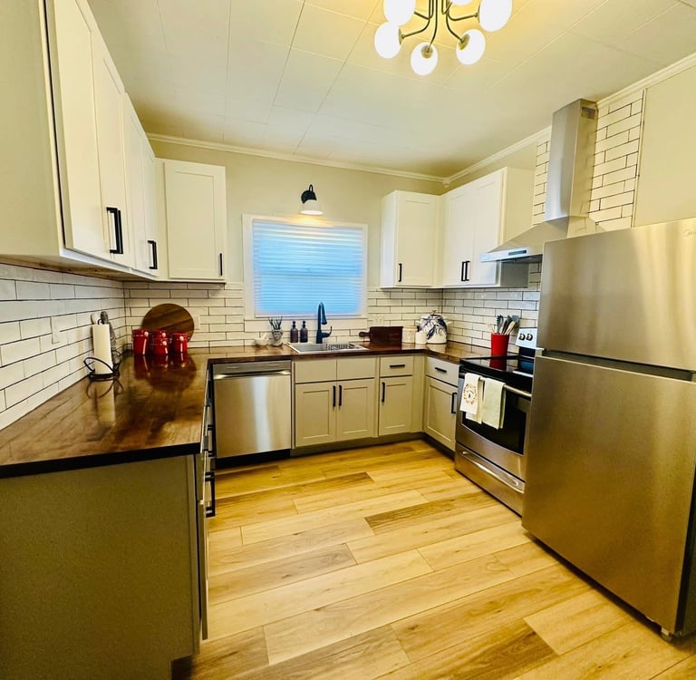 Modern kitchen with white upper cabinets, stainless steel appliances, and butcher block countertops.