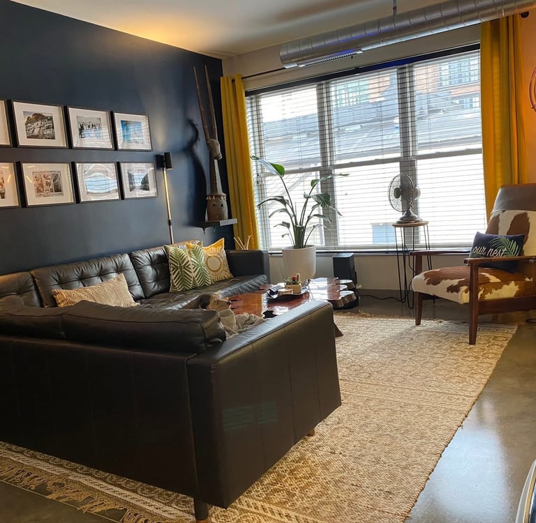 Modern industrial living room featuring a black leather sectional sofa, gallery wall, and cowhide chair.