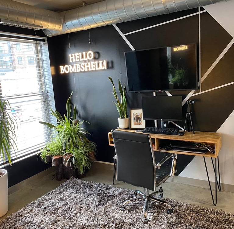 Ohio staged Modern home office with a wooden desk, black accent wall, neon sign, and indoor plants.