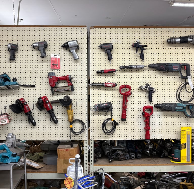 A collection of electric power tools and pneumatic equipment hanging on a pegboard workshop wall.