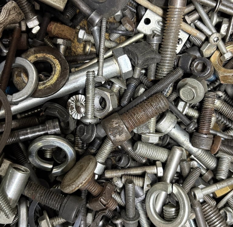 Top view of a disorganized pile of various metal fasteners, including steel bolts, nuts, screws, and washers.