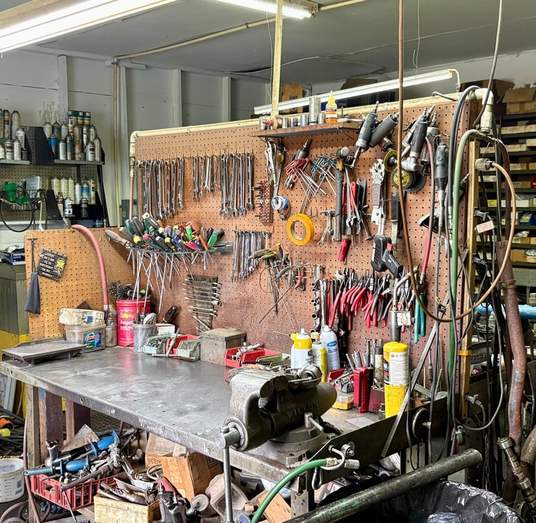 Organized mechanical workshop with hand tools on pegboards above a metal workbench with a vise.