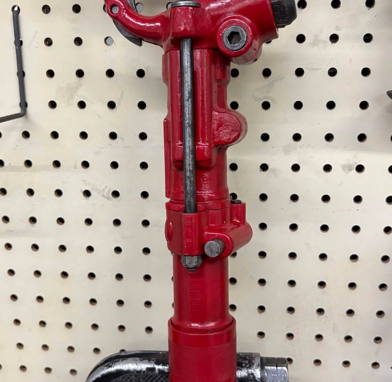 Red industrial pneumatic rivet buster tool hanging on a pegboard in a workshop.