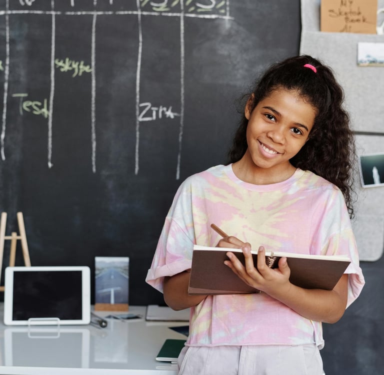 Menina adolescente sorridente segurando um caderno e lápis em frente a um quadro negro com cronograma semanal organizado